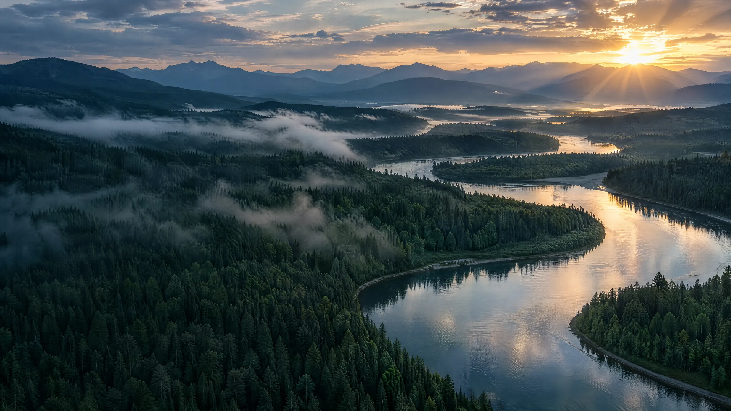 Aerial view of a river winding through misty forest at sunrise
